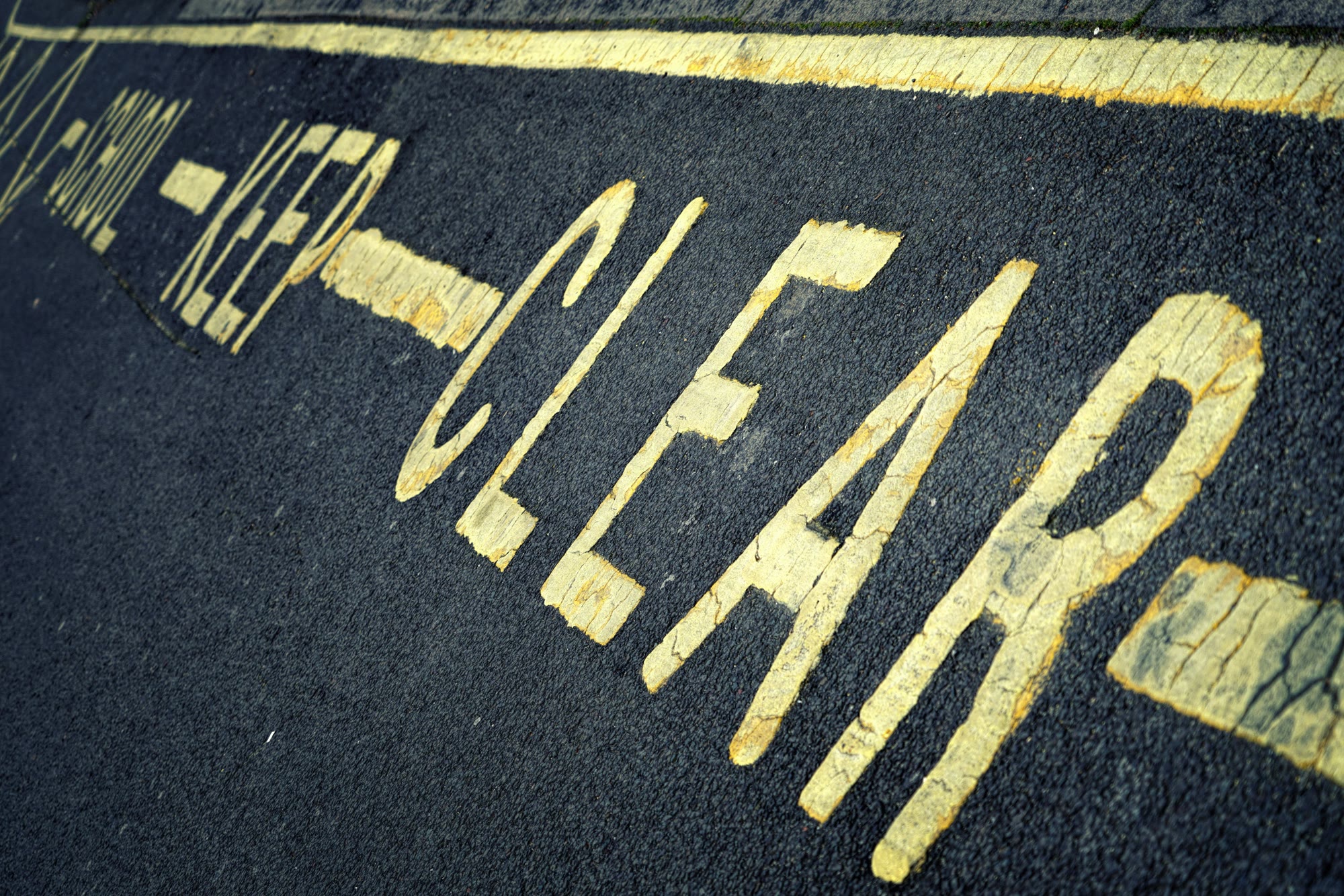 Yellow painted words on dark pavement reading keep clear.