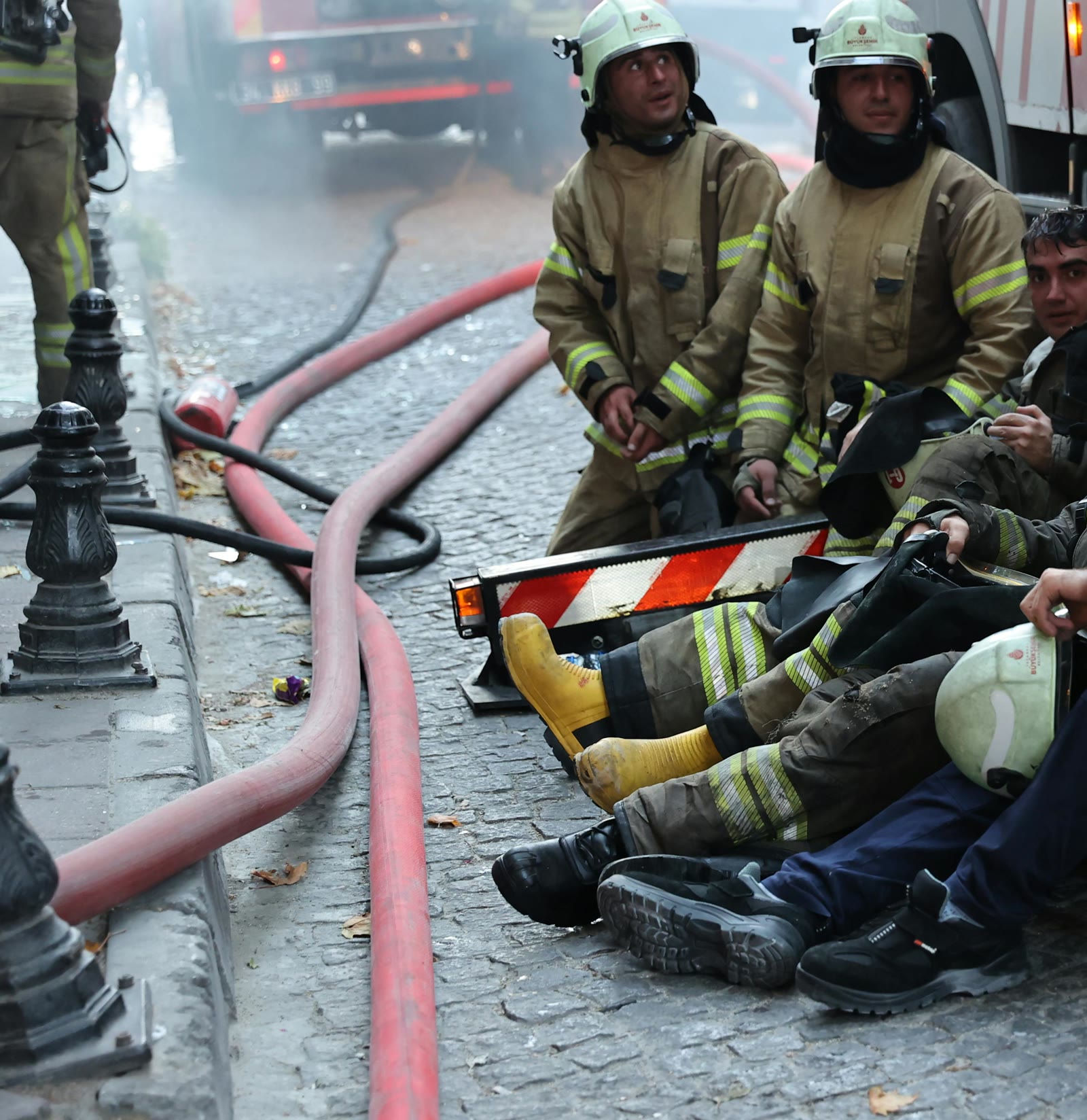 Firefighters resting beside hoses after an incident.